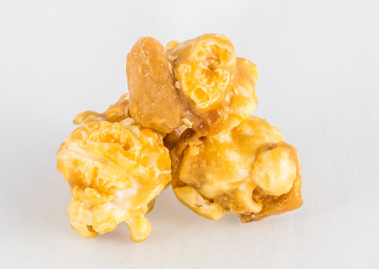 A pile of three pieces of caramel-coated popped popcorn with a cashew.