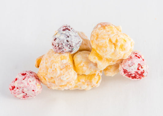 A stack with two pieces of white chocolate-covered popcorn with three berry-flavored cereal balls.